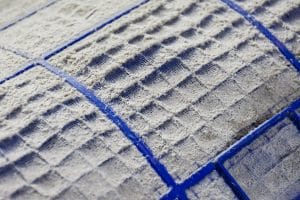 Close-up of a heavily dust-covered HVAC air filter, with thick white buildup obscuring much of the blue filter grid.