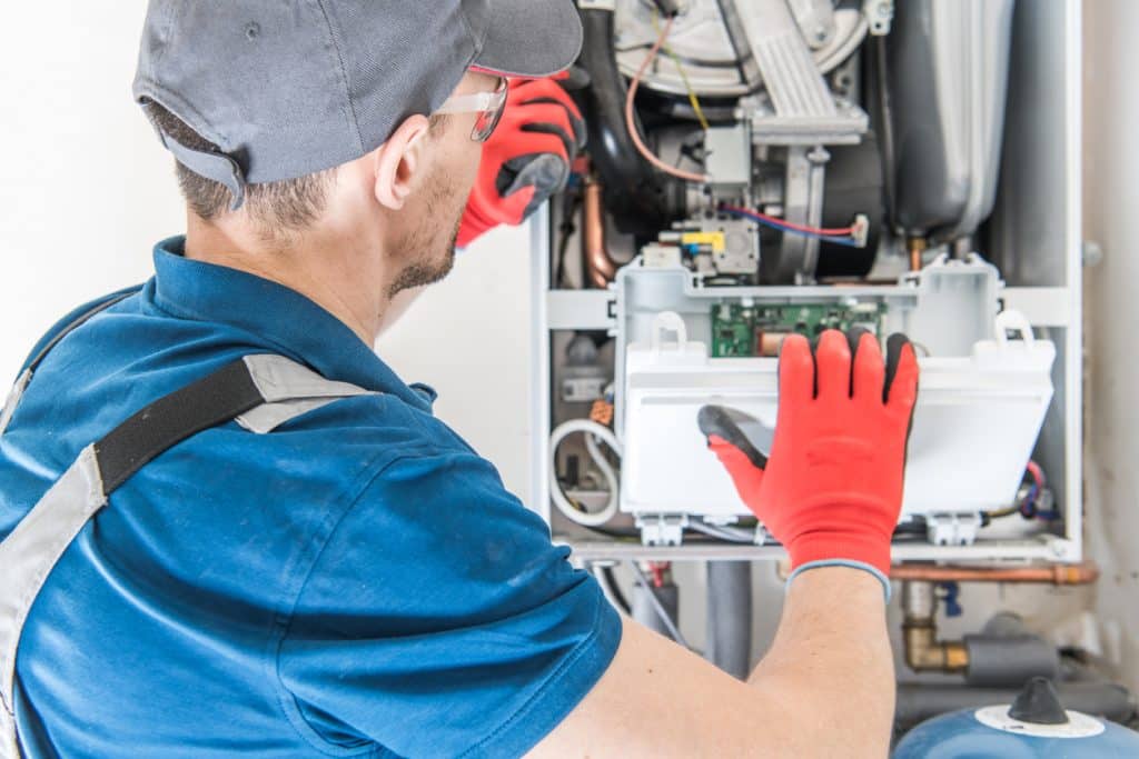 HVAC technician inspecting and repairing an open furnace unit with exposed components and wiring.